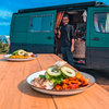 Une assiette de riz et légumes au premier plan, un homme debout dans l'ouverture de la porte d'un van vert en arrière-plan