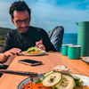 Homme avec lunettes assis à une table avec de la nourriture et buvant d'une tasse en plein air