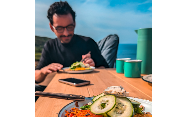 Homme avec lunettes assis à une table avec de la nourriture et buvant d'une tasse en plein air