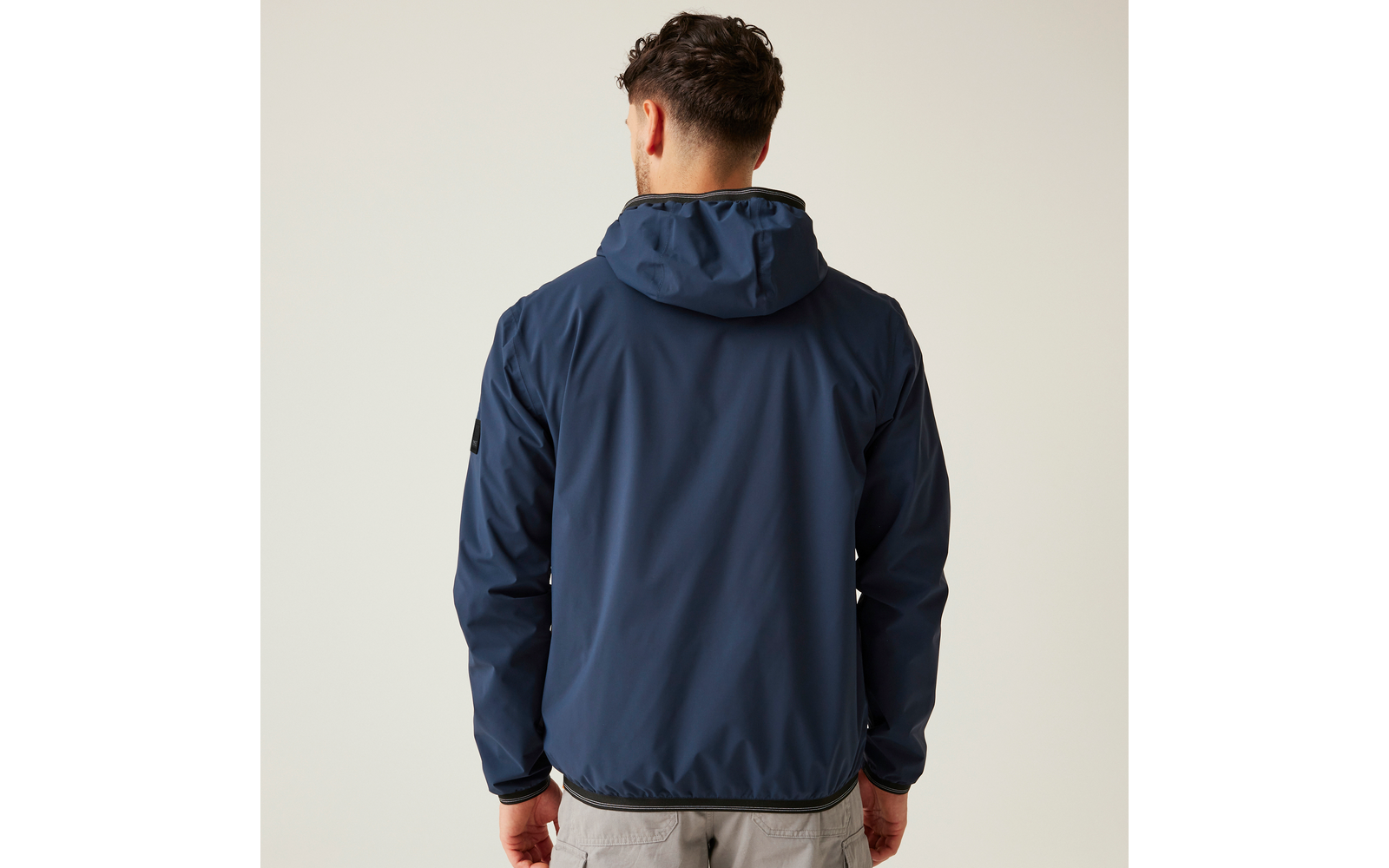 Person von hinten in dunkelblauer Kapuzenjacke und hellgrauer Hose vor hellem Hintergrund