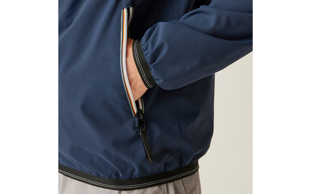 Nahaufnahme einer dunkelblauen Jacke mit zippbarer Seitentasche, in die eine Hand gesteckt ist; sichtbarer Reißverschluss mit mehrfarbigem Besatz und schwarzem Zipper, elastischer Saum und Ärmelbund, graue Hose sichtbar