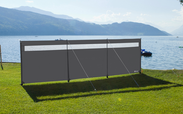 Protector contra el viento gris en un prado frente a un lago con montañas al fondo