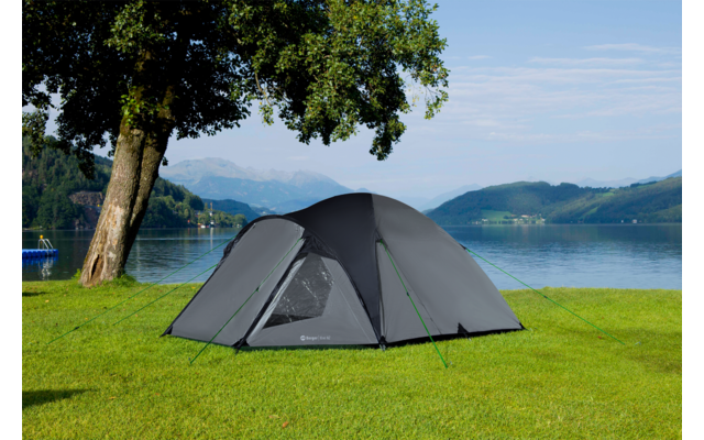 Graues Zelt auf einer grünen Wiese neben einem See mit Bergen im Hintergrund