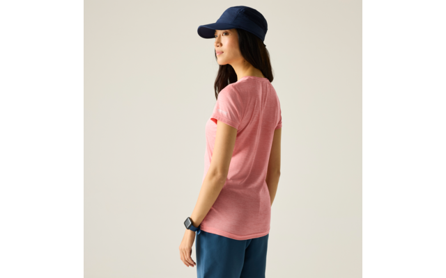 Persoon in roze T‑shirt, donker lang haar, donkerblauwe pet, donkerblauwe broek, smartwatch om linkerpols, iets weggedraaid tegen een lichte achtergrond