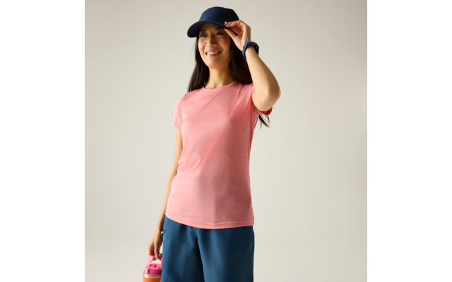 Vrouw in roze T-shirt en donkerblauwe pet, houdt een roze drinkfles vast, draagt blauwe shorts en een polshorloge, effen lichte achtergrond