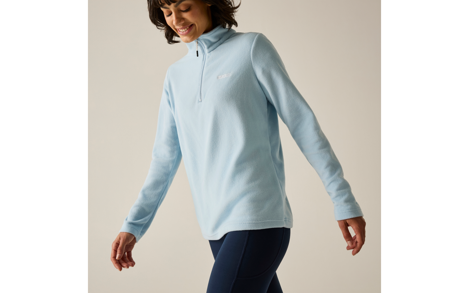 Persona con pile azzurro chiaro con mezza cerniera e leggings blu scuro, sorridente e con lo sguardo rivolto verso il basso