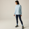 Persona in profilo su sfondo chiaro, indossa un maglione azzurro con mezza cerniera, leggings blu scuro, calzini azzurri e scarpe da trekking grigie