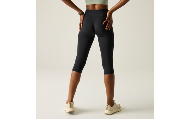 Rear view of a person wearing black capri leggings, a light green crop top and beige sneakers, hands on hips, light background