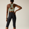 Person from behind, light green sports bra, black capri leggings, right hand on lower back, braided hair tied up