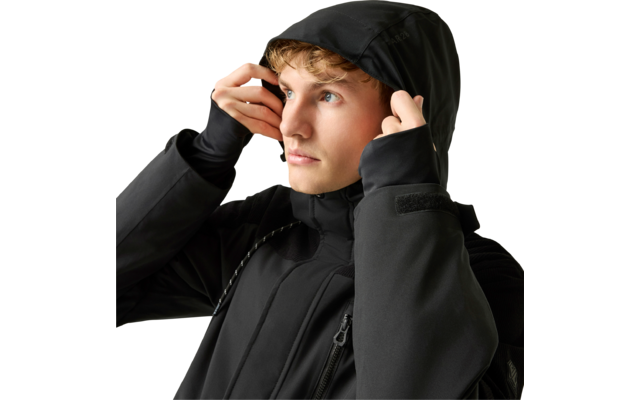 Junger Mann zieht die Kapuze einer schwarzen Jacke über den Kopf, blickt nach oben rechts, heller Hintergrund