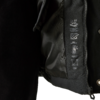 Nahaufnahme eines geöffneten schwarzen Jackets mit Innenfutter, Reißverschluss, Druckknopf, aufgedruckten Pflegesymbolen und einem Teil eines schwarzen, gerippten Ärmels