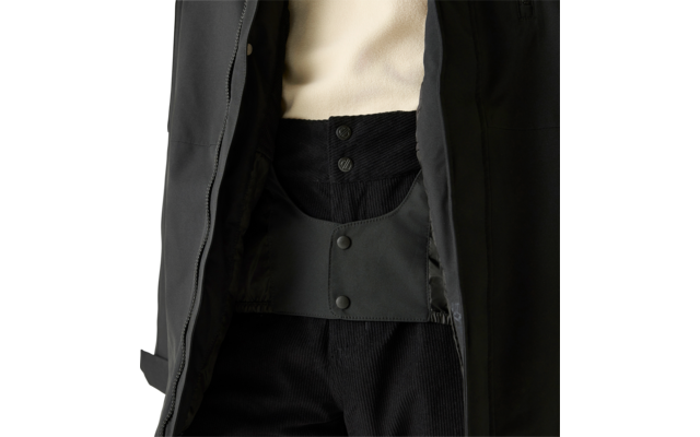 Nahaufnahme eines geöffneten schwarzen Mantels über einem cremefarbenen Pullover und einer schwarzen Hose mit sichtbarer Knopfleiste