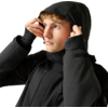 Junger Mann zieht die Kapuze einer schwarzen Jacke über den Kopf, blickt nach oben rechts, heller Hintergrund