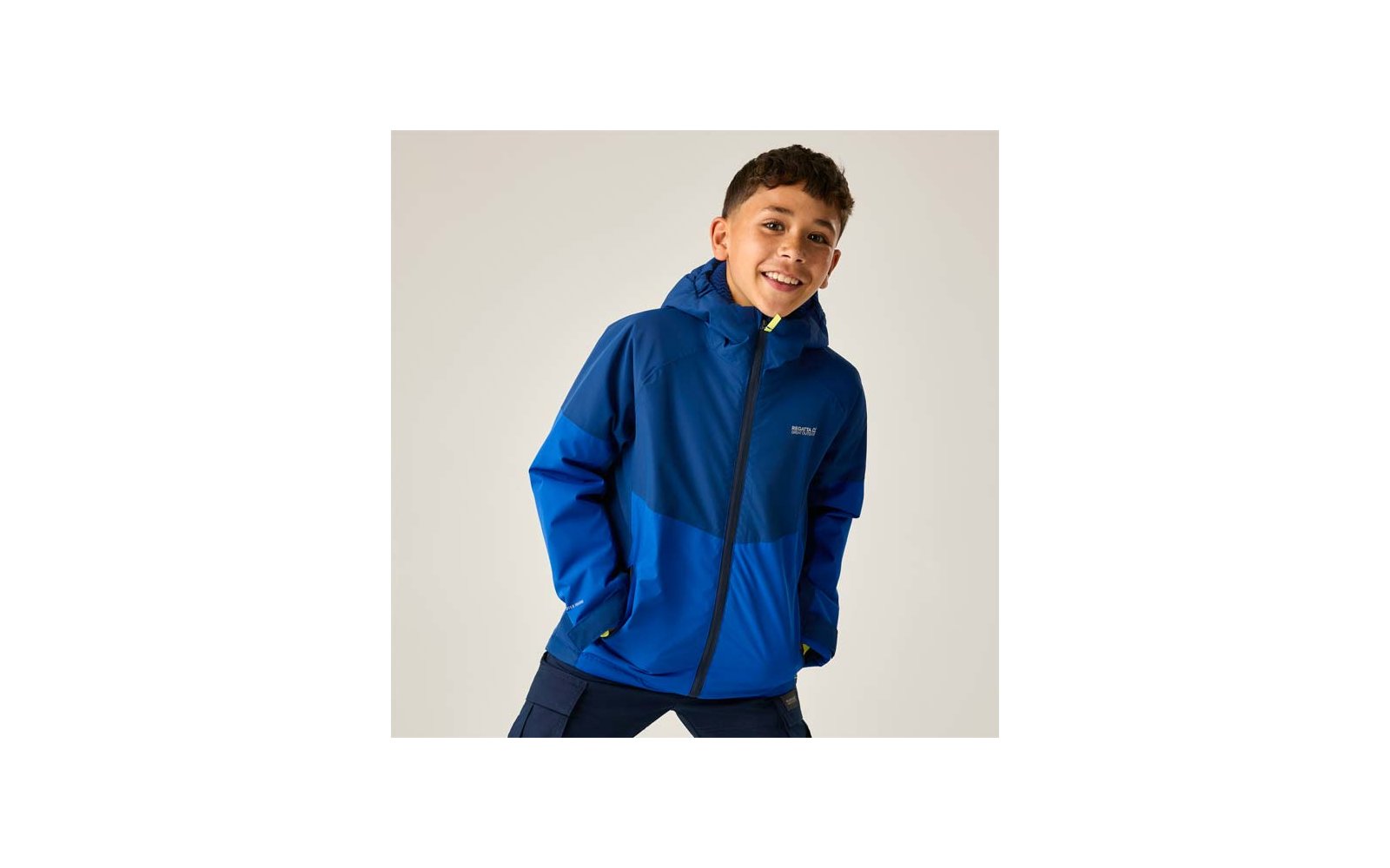 Junge mit blauer Kapuzenjacke, Hände in den Taschen, leicht nach vorn geneigt vor hellem Hintergrund