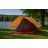 Bâche orange au-dessus d'une tente rouge en mesh, montée sur l'herbe au bord d'un lac ; tronc d'arbre à droite, forêt et ciel bleu en arrière-plan