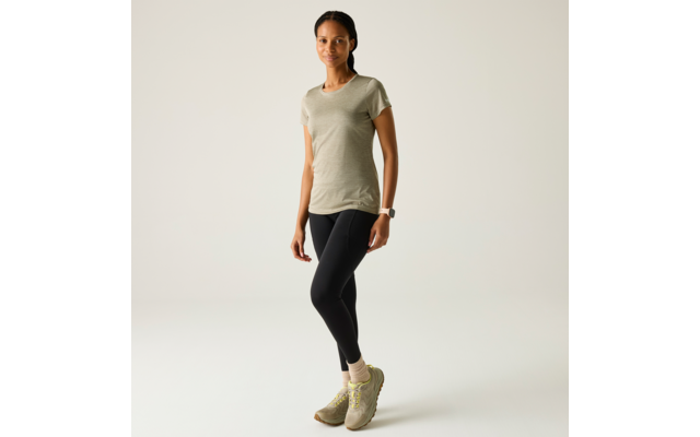 Persoon staat voor een lichte achtergrond, draagt een olijfgroen T‑shirt, zwarte legging, lichte sokken en groenachtige sportschoenen, smartwatch om linkerpols, haar naar achteren gebonden