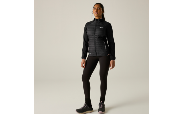 Persona in piedi, rivolta in avanti, indossa giacca nera trapuntata con cerniera, leggings neri e scarpe sportive nere, sfondo chiaro uniforme