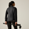 Persona vista da dietro con giacca nera trapuntata e leggings, tiene due bastoncini da trekking ripiegati dietro la schiena, sfondo chiaro uniforme