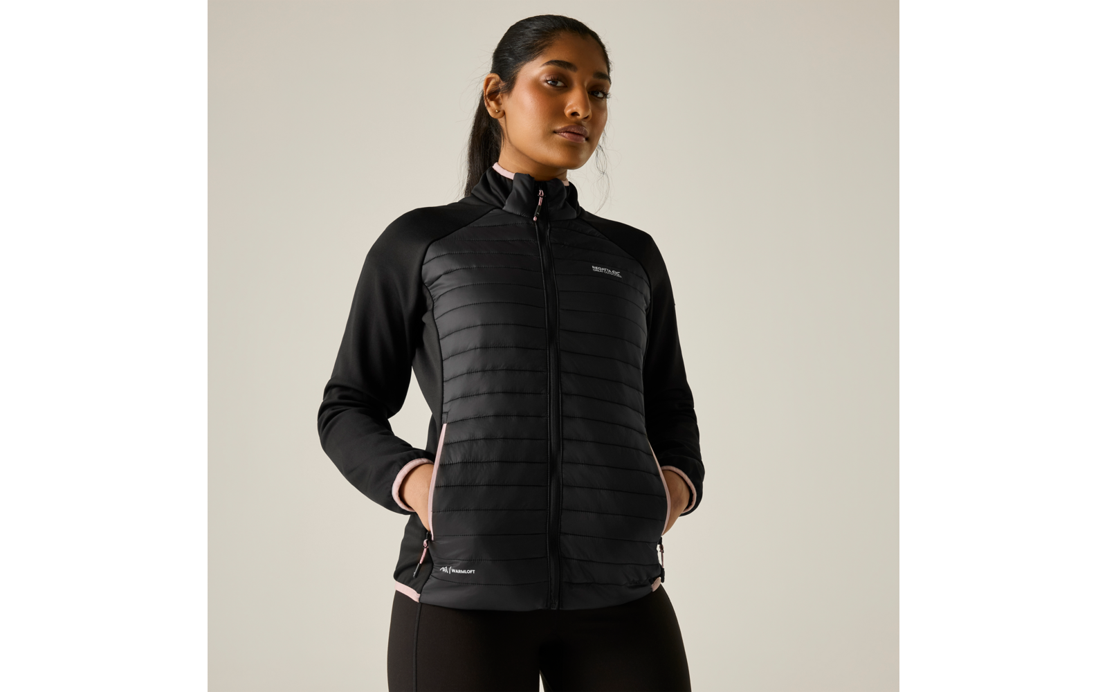 Persona con giacca trapuntata nera con cerniera, mani nelle tasche, davanti a uno sfondo chiaro