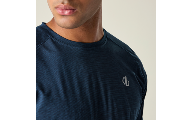 Buste et partie inférieure du visage d'une personne portant un T‑shirt bleu foncé avec un petit logo blanc sur la poitrine gauche, fond gris clair