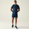 Homme debout en t‑shirt bleu foncé, short bleu foncé et baskets sur fond clair, mains dans le dos