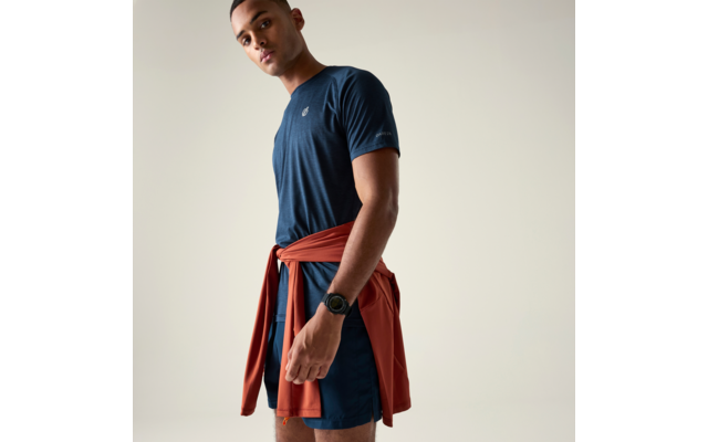 Personne portant un t-shirt et un short bleu marine, une veste couleur rouille nouée à la taille, une montre-bracelet, fond clair uni