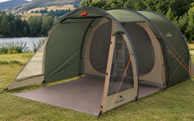 Groene campingtent met open voortent en grondzeil op gras, meer, bomen en heuvels op de achtergrond