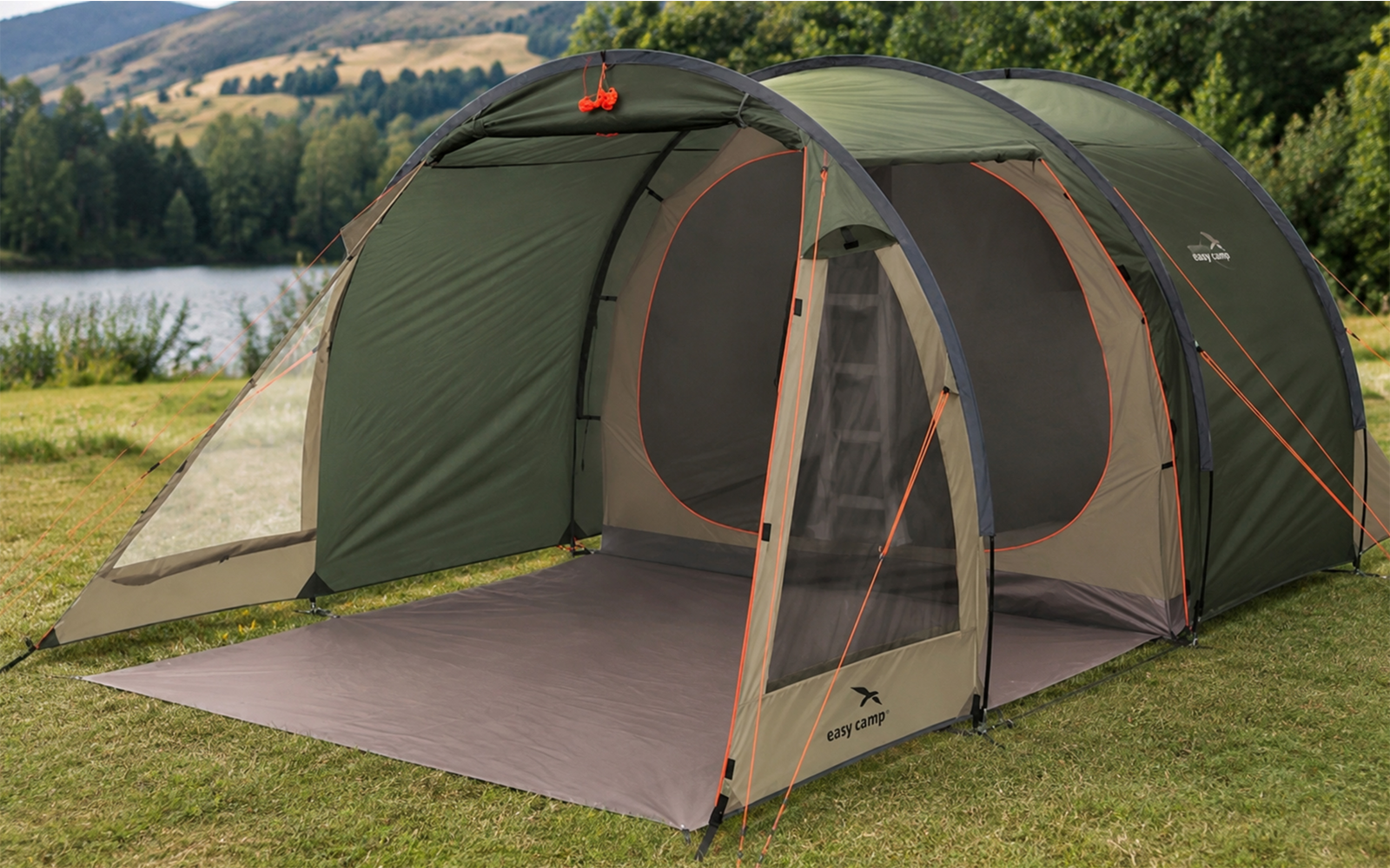 Groene campingtent met open voortent en grondzeil op gras, meer, bomen en heuvels op de achtergrond