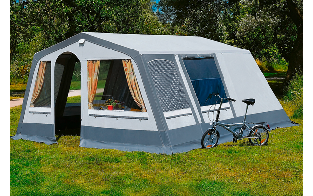 Grote grijs-witte tent op gras, twee ramen met gordijnen en bloempotten, open ingang, fiets leunt tegen de buitenkant, bomen op de achtergrond