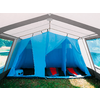 Binnenkant van een grote blauwe tent met open voorkant, drie slaapcabines, twee zichtbare rode slaapmatten en een blauwe koelbox op het gras