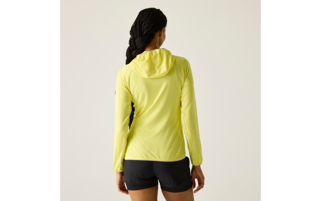 Person von hinten, trägt gelbe Kapuzenjacke und schwarze Shorts, geflochtene Haare, steht vor hellem Hintergrund