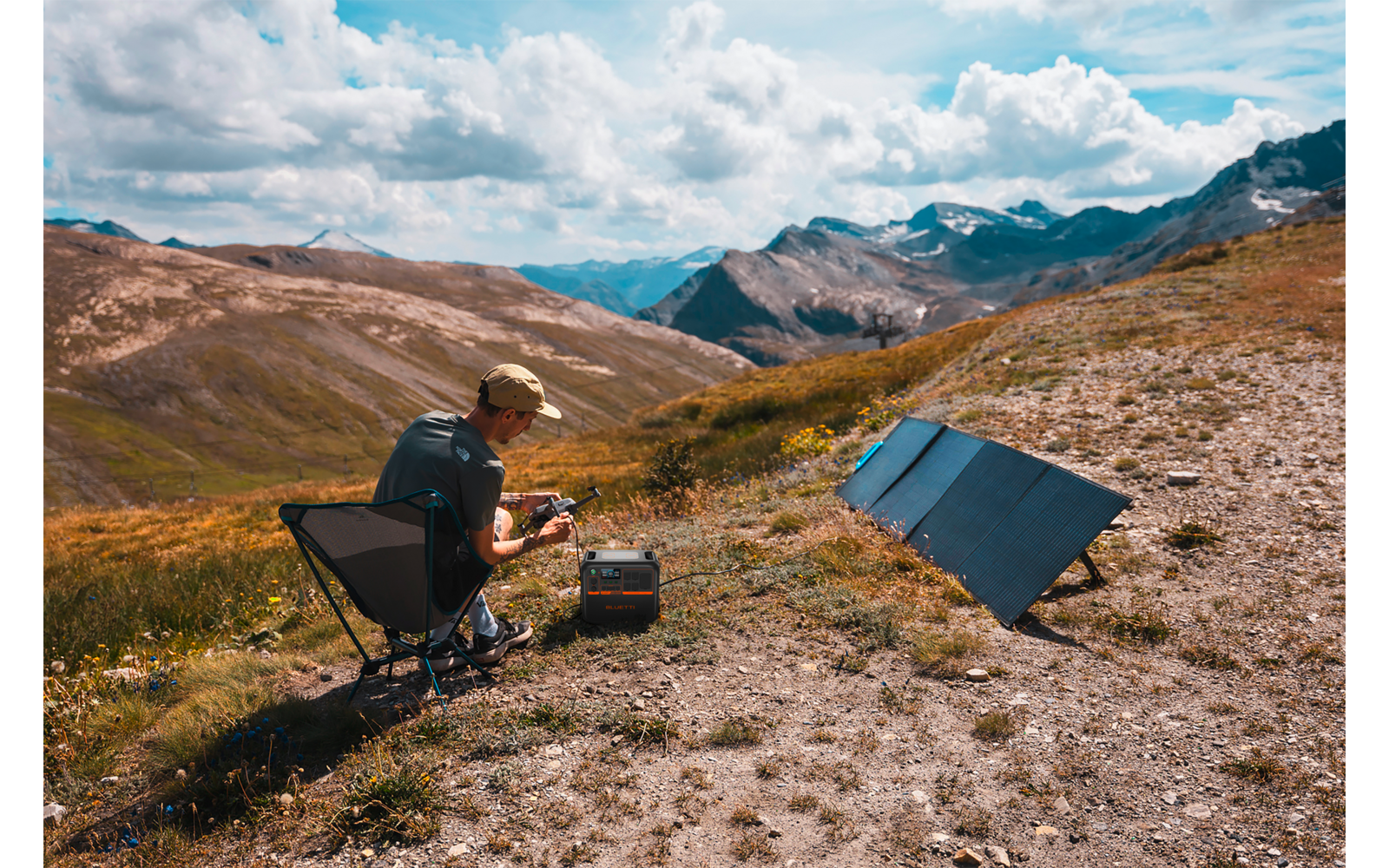 Person sitzt auf einem Stuhl in einer Berglandschaft mit einem offenen Koffer vor sich