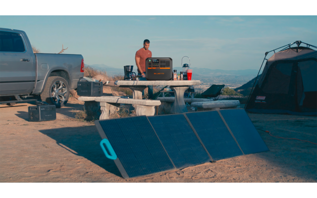 Zwei Personen und zwei Fahrzeuge neben ausgebreiteten Solarpaneelen im Freien