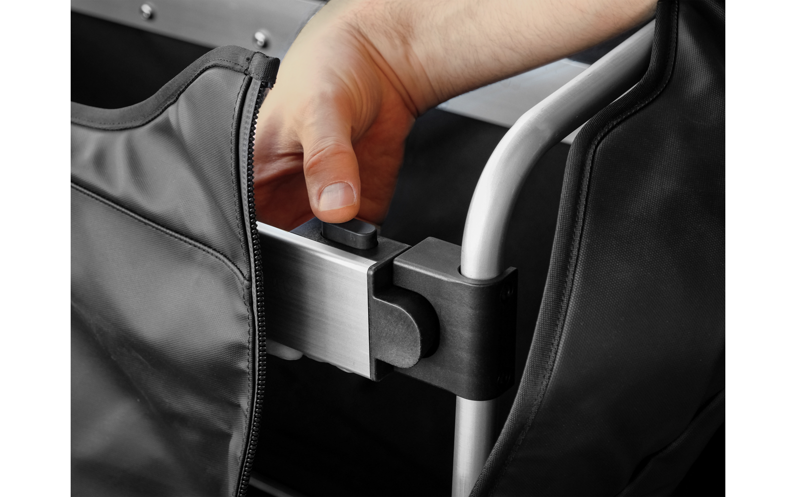 Hand greift schwarzen runden Knopf an einem silbernen Metallrohr; schwarzer Stoff mit Reißverschluss sichtbar