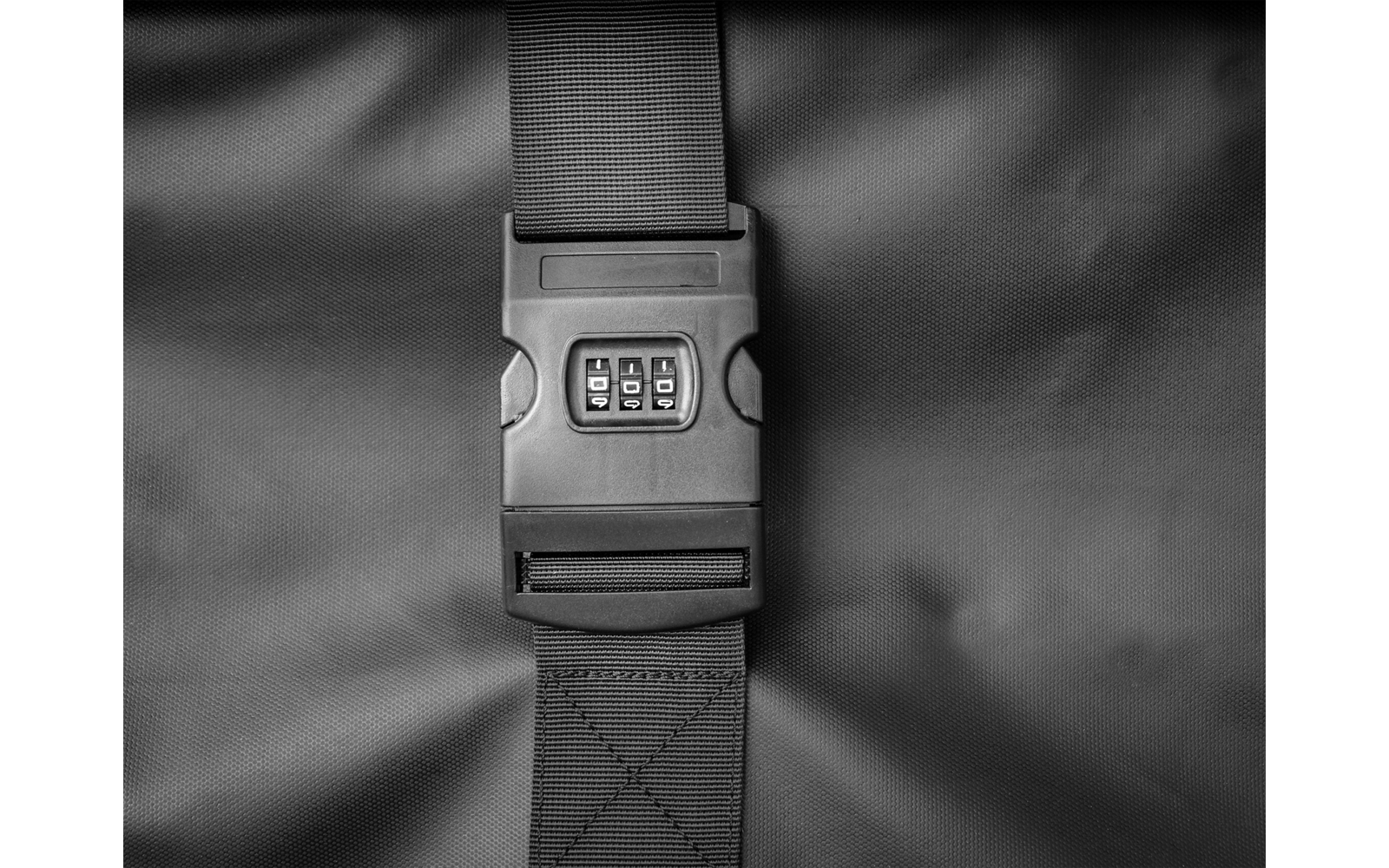 Schwarzer Gepäckgurt mit Zahlenschloss mittig auf dunklem Stoff