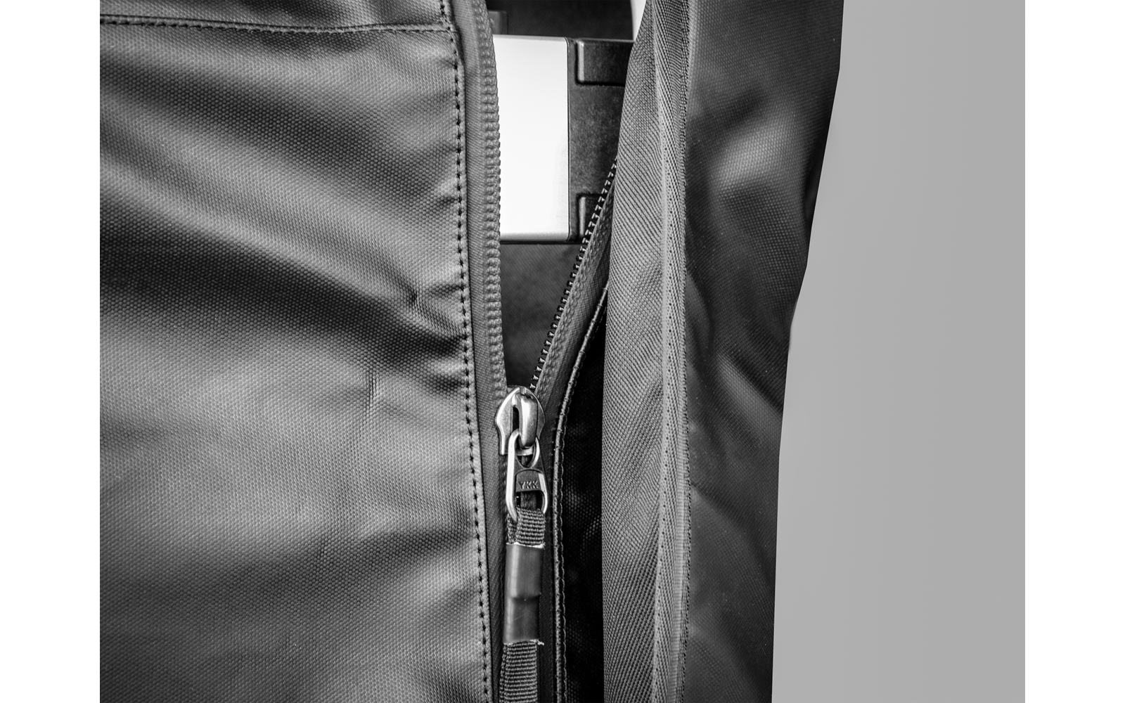 Nahaufnahme eines teilweise geöffneten Reißverschlusses an dunklem Stoff mit sichtbarem Zipper und Nähten