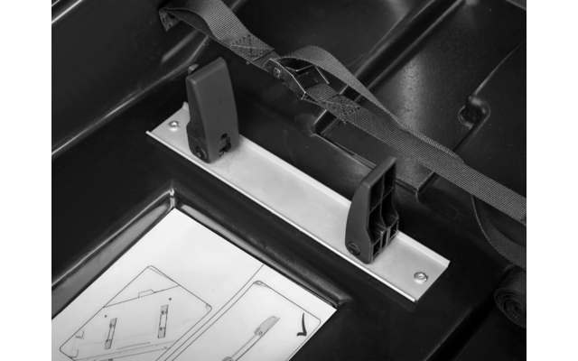 Schwarzer Kunststoffinnenraum mit Metallstange, zwei schwarzen Halterungen, einem Gurt und einem Blatt mit Diagrammen