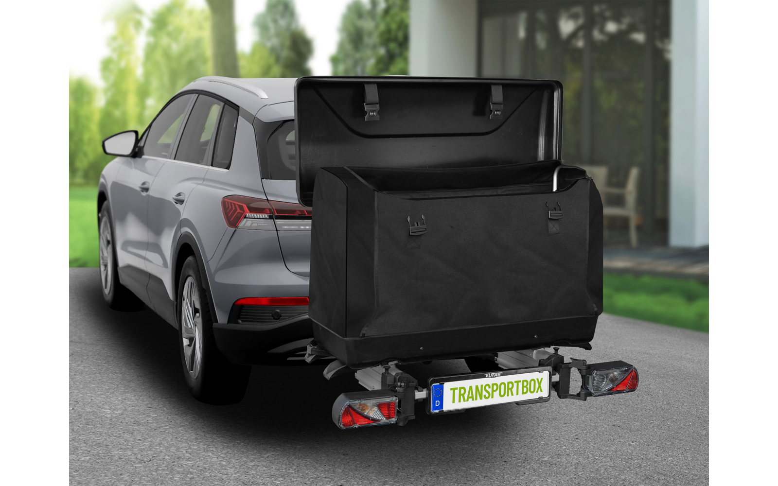 Grauer SUV in Einfahrt vor Haus, am Heck eine offene schwarze Transportbox auf der Anhängerkupplung, Kennzeichen "TRANSPORTBOX", Bäume und Hauseingang im Hintergrund