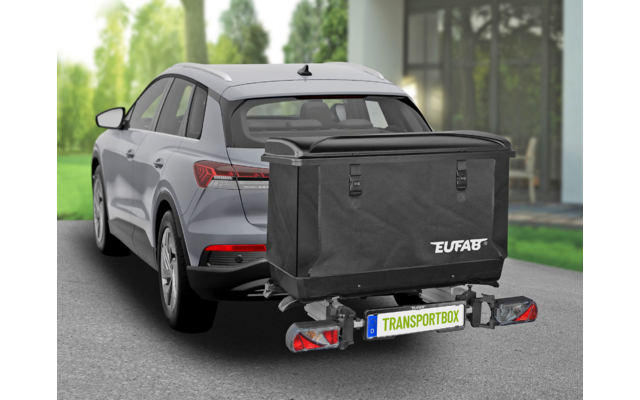 Grijze SUV vanaf achter-links, zwarte transportbox op de trekhaak met opschrift 'EUFAB' en kenteken 'TRANSPORTBOX', achterlichten, oprit, huis met glazen gevel en bomen op de achtergrond