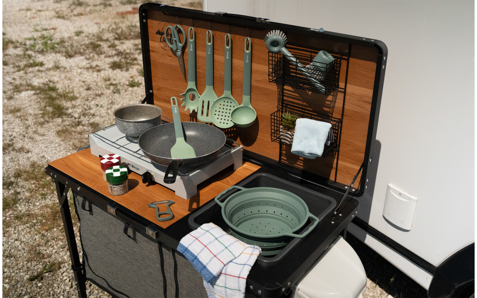 Campingtisch mit Geschirr, Töpfen und Küchenutensilien vor einem Wohnmobil