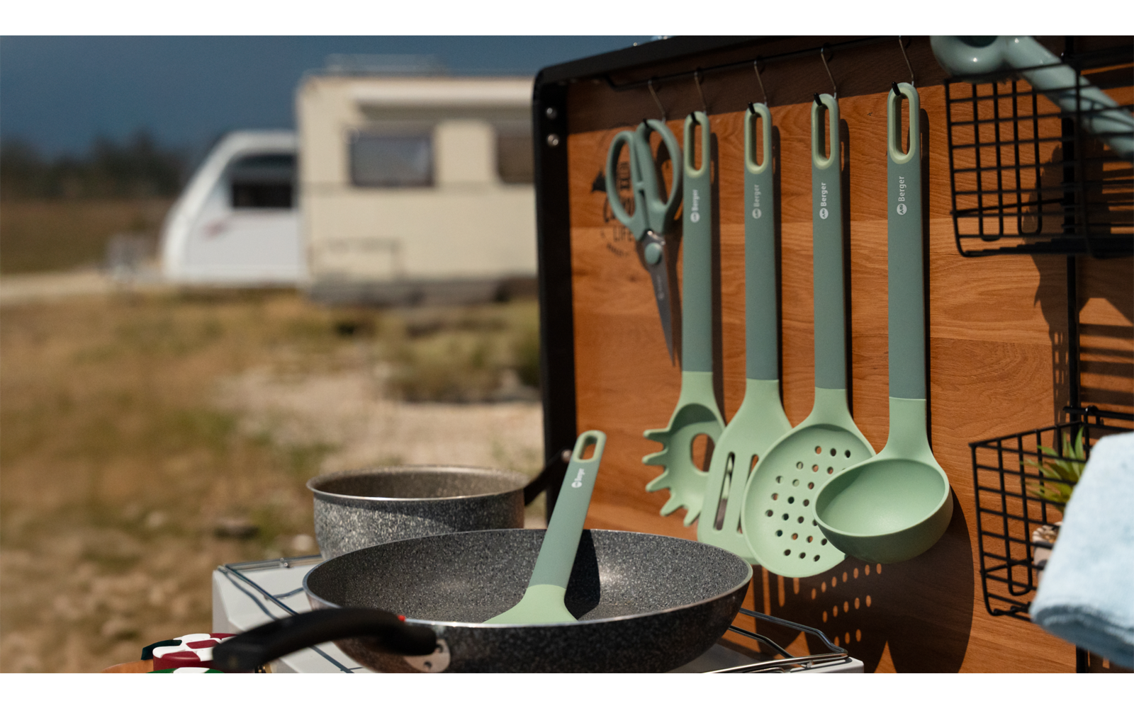 Camping-Küche mit Kochtöpfen, Pfannen und Küchenutensilien vor Wohnwagen
