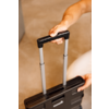 Mains tenant la poignée télescopique sortie d'une valise noire, sol beige en arrière-plan