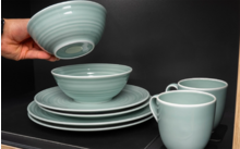 Main tenant un bol au-dessus de vaisselle turquoise empilée dans une armoire