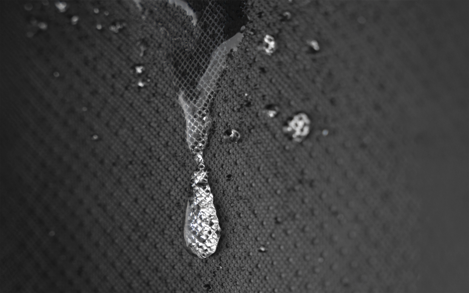 Nahaufnahme eines Wassertropfens und eines dünnen Wasserfilms auf einer dunklen, strukturierten Oberfläche