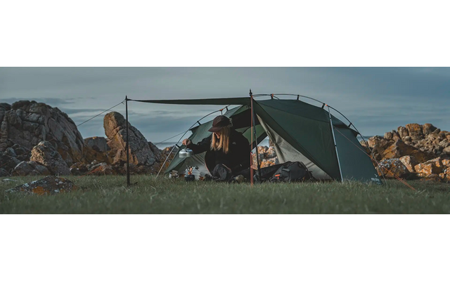 Ein grünes Zelt steht auf einer Wiese mit Felsspitzen im Hintergrund