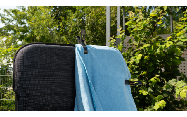 Schwarzer Koffer mit einem blauen Handtuch darauf, im Hintergrund grüne Pflanzen