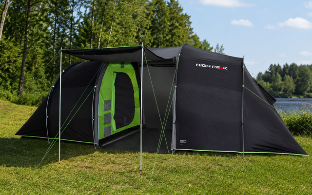 Zwarte tent met open ingang en groen binnenzeil, opgezet op gras, op de achtergrond bomen, een meer en een blauwe lucht met wolken