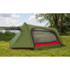 Green tent with red accents and a mesh side window on grass, lake and trees in the background under a partly cloudy sky