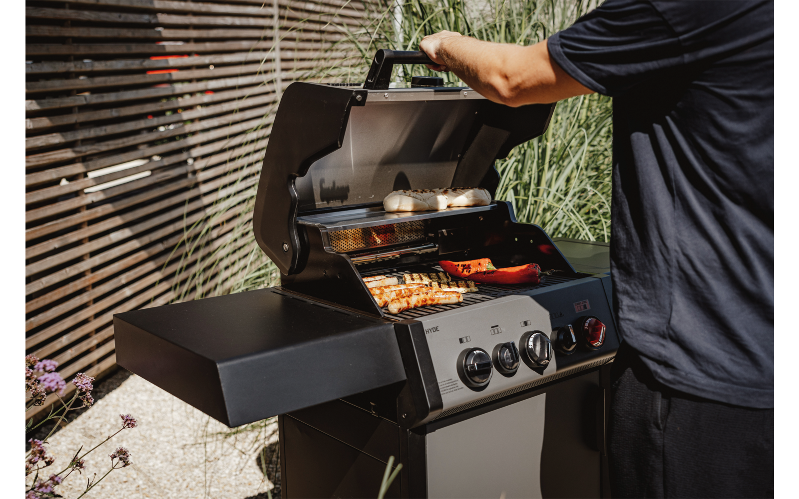 Person grillt Würstchen und Fleisch auf einem Gasgrill auf einem Balkon