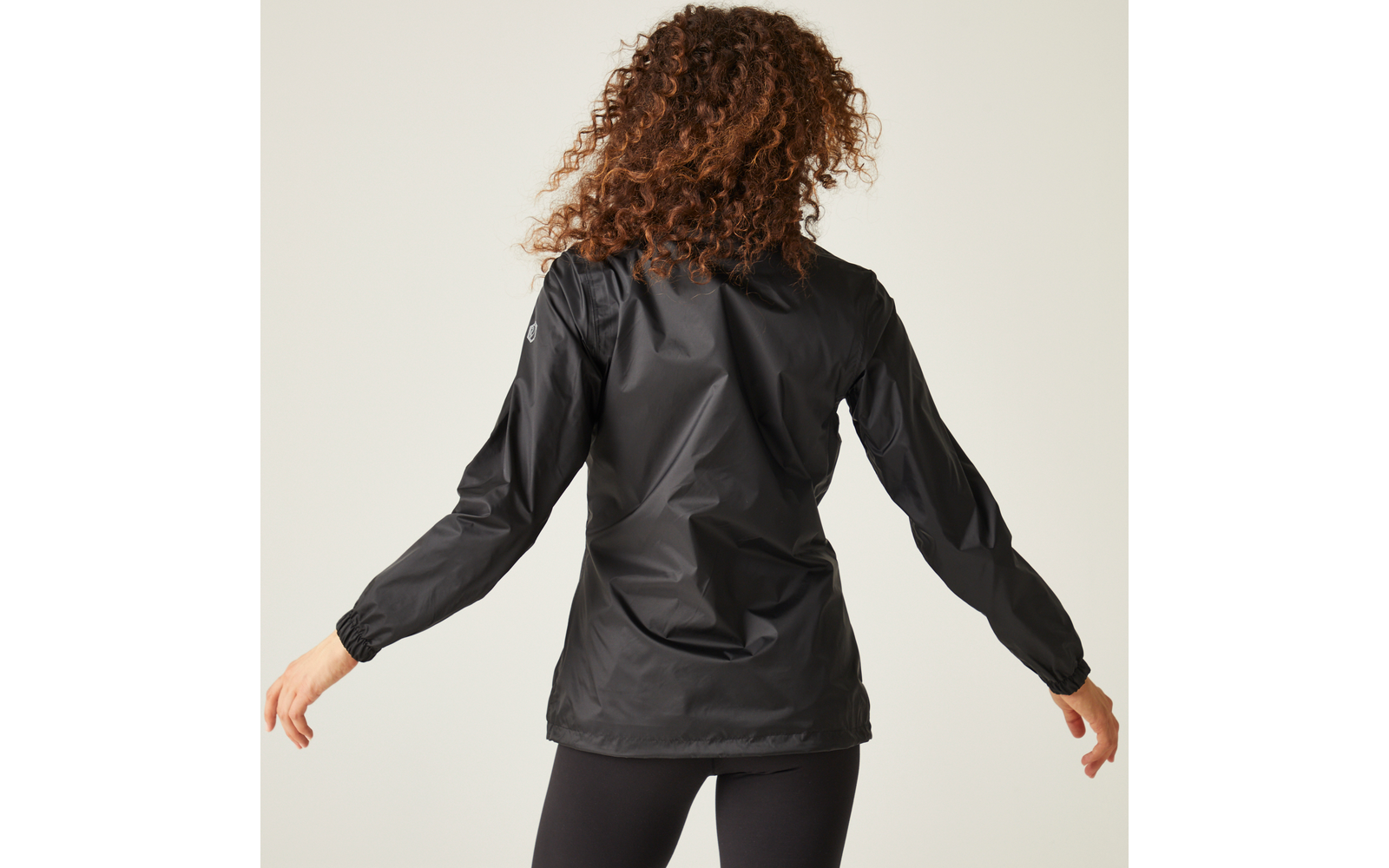 Persona vista di spalle con giacca nera e leggings neri, capelli ricci, su sfondo chiaro
